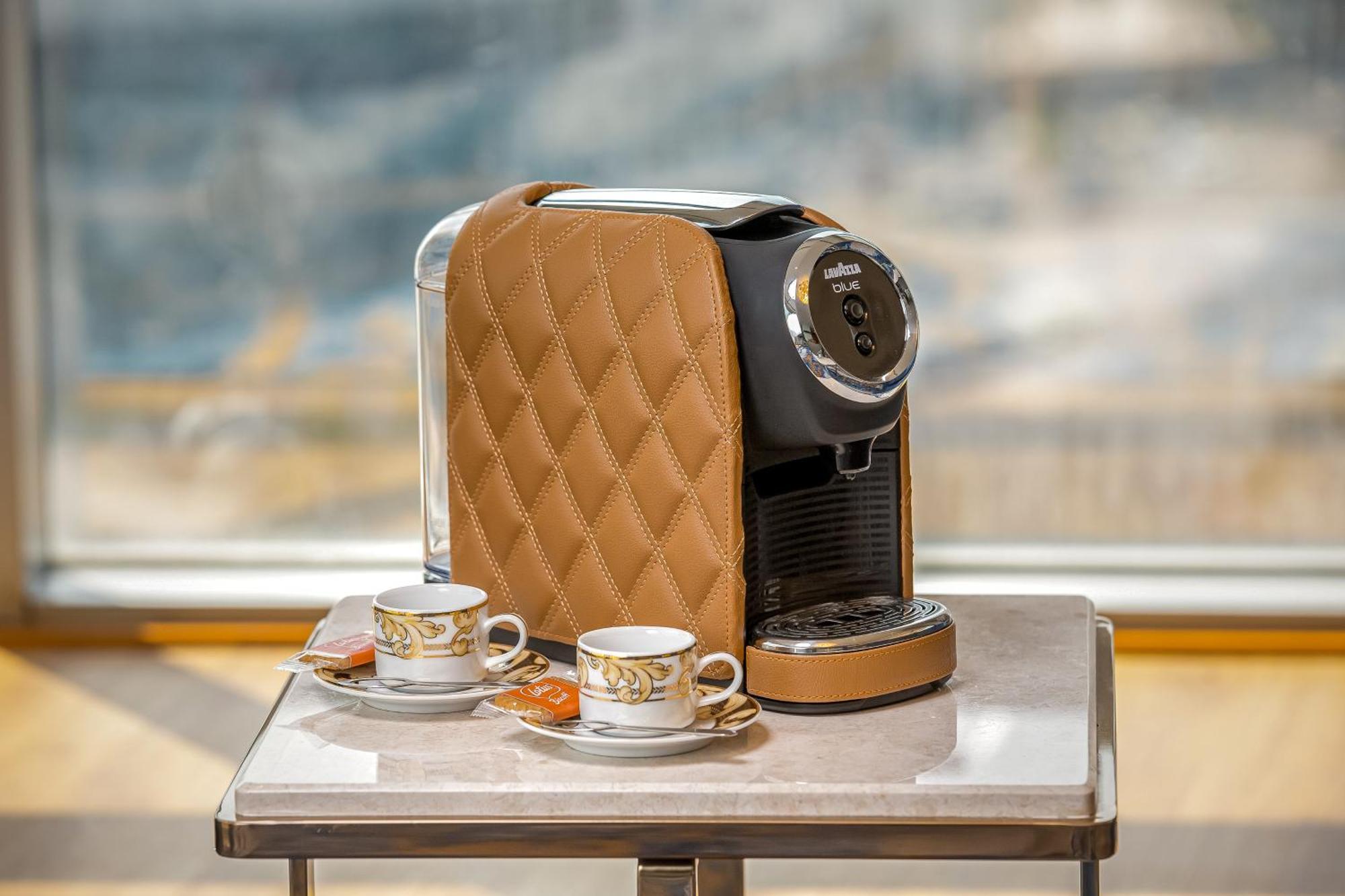 Golden Sands Boutique Hotel-Dubai Creek Екстериор снимка The photo shows a stylish coffee machine with a quilted brown cover, placed on a table. Beside it are two elegant cups of coffee, each accompanied by small plates with a biscuit or cookie. The background appears to have a bright, airy setting, possib