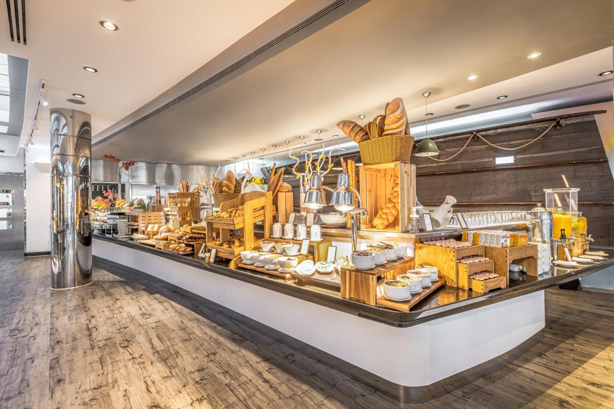Golden Sands Boutique Hotel-Dubai Creek Екстериор снимка The image shows a buffet setup featuring an array of food items displayed on a sleek counter. There are various baked goods, including bread and pastries, along with different types of cheeses and spreads. The setting appears elegant, with modern des