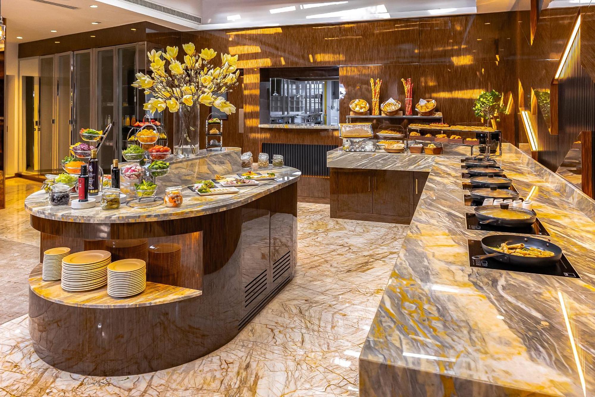 Golden Sands Boutique Hotel-Dubai Creek Екстериор снимка The photo shows an elegantly designed dining area or buffet setup. There are large, polished marble surfaces with a variety of food items displayed. One main island features a selection of fresh fruits and colorful dishes, surrounded by decorative el
