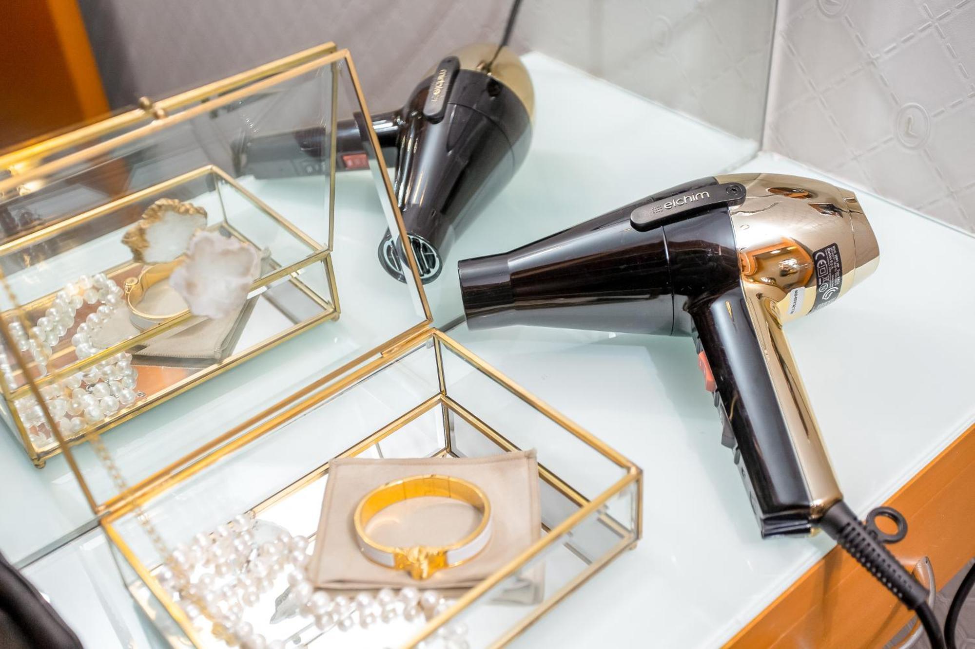 Golden Sands Boutique Hotel-Dubai Creek Екстериор снимка The photo depicts a stylish bathroom or vanity setup featuring a hairdryer and some jewelry. The hairdryer is predominantly black with gold accents, placed on a light-colored surface. Nearby, there is a glass jewelry box with gold trim, containing va