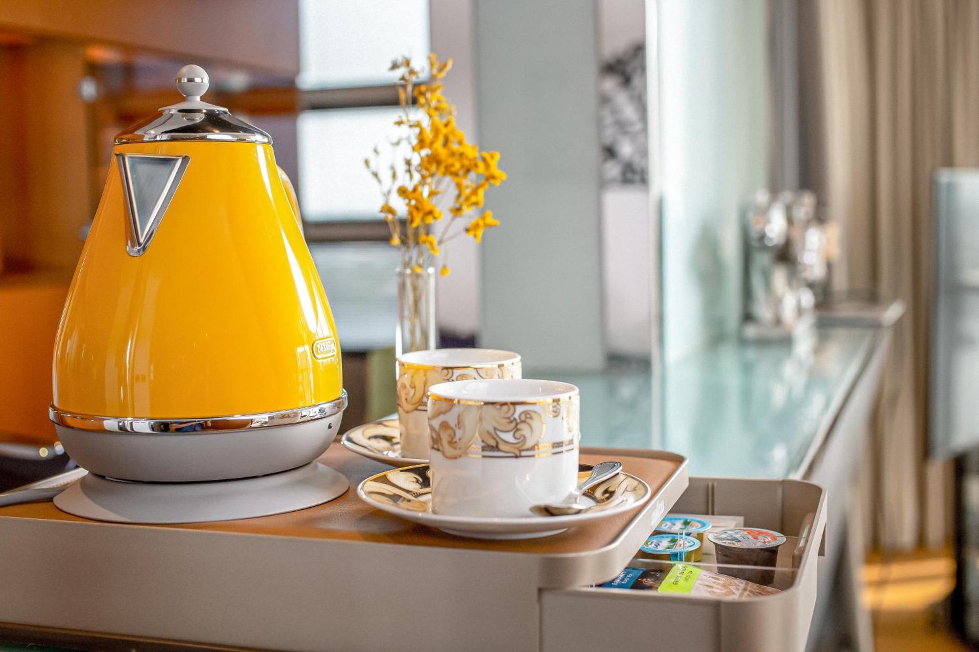 Golden Sands Boutique Hotel-Dubai Creek Екстериор снимка The photo shows a stylish setup featuring a bright yellow kettle with a chrome accent, placed on a tray. Accompanying the kettle are two elegant tea or coffee cups, each resting on saucers. There is also a small vase containing yellow flowers, adding