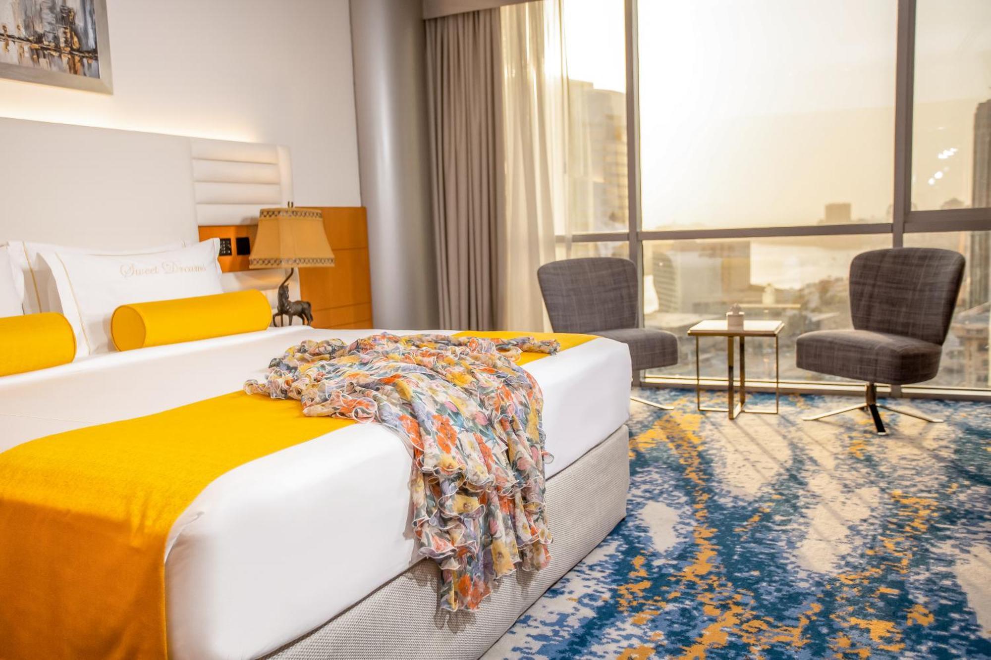 Golden Sands Boutique Hotel-Dubai Creek Екстериор снимка The photo shows a modern hotel room featuring a spacious bed with a white and orange color scheme. A colorful throw blanket is draped across the bed. Next to the bed, there is a lamp and some decorative elements. The room has large windows allowing n