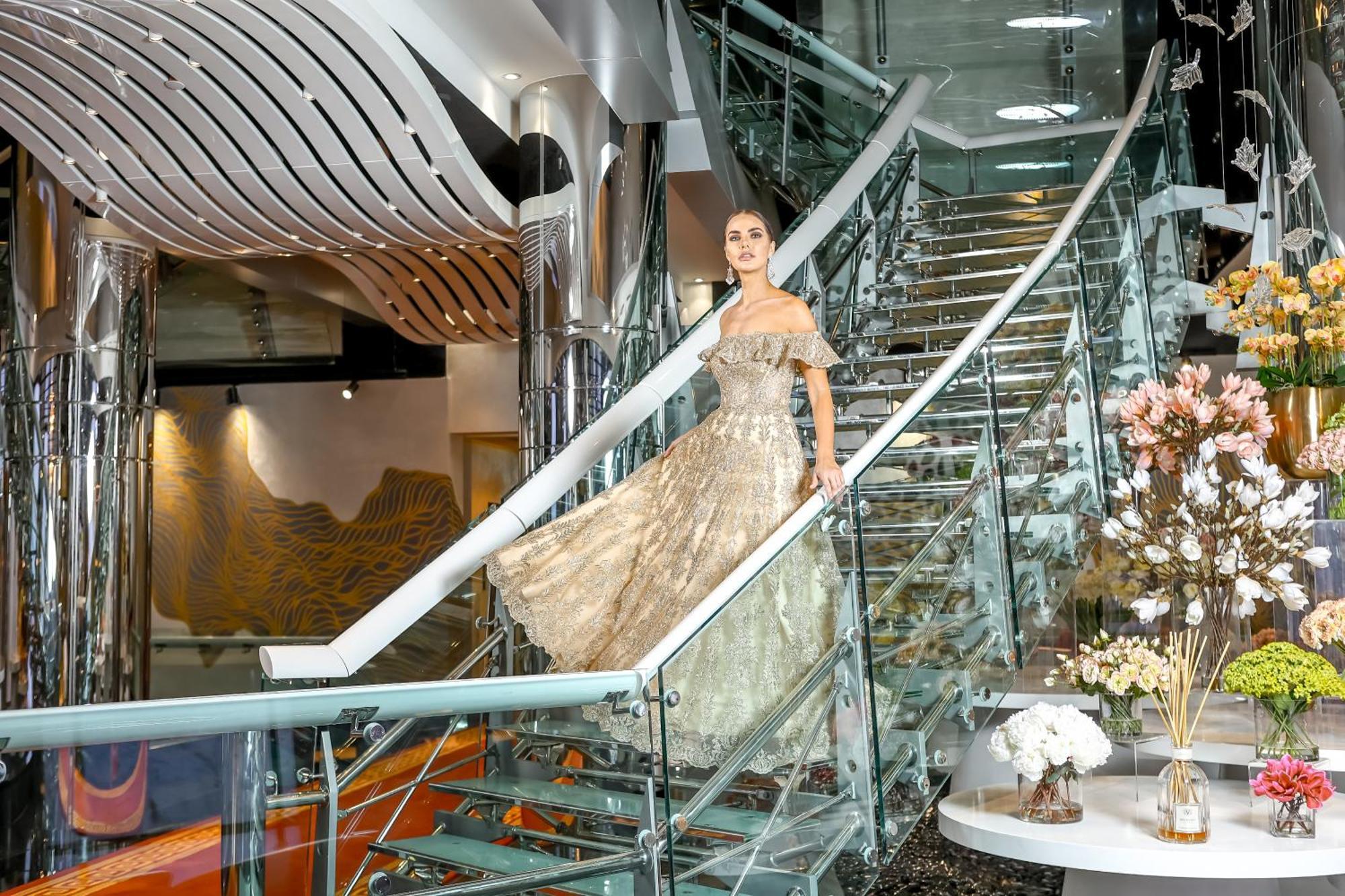 Golden Sands Boutique Hotel-Dubai Creek Екстериор снимка The photo depicts a woman gracefully descending a modern, curved staircase. She is wearing an elegant, off-the-shoulder gown that has a light, flowing design. The staircase is made of glass and metal, featuring a sleek and contemporary style. In the 