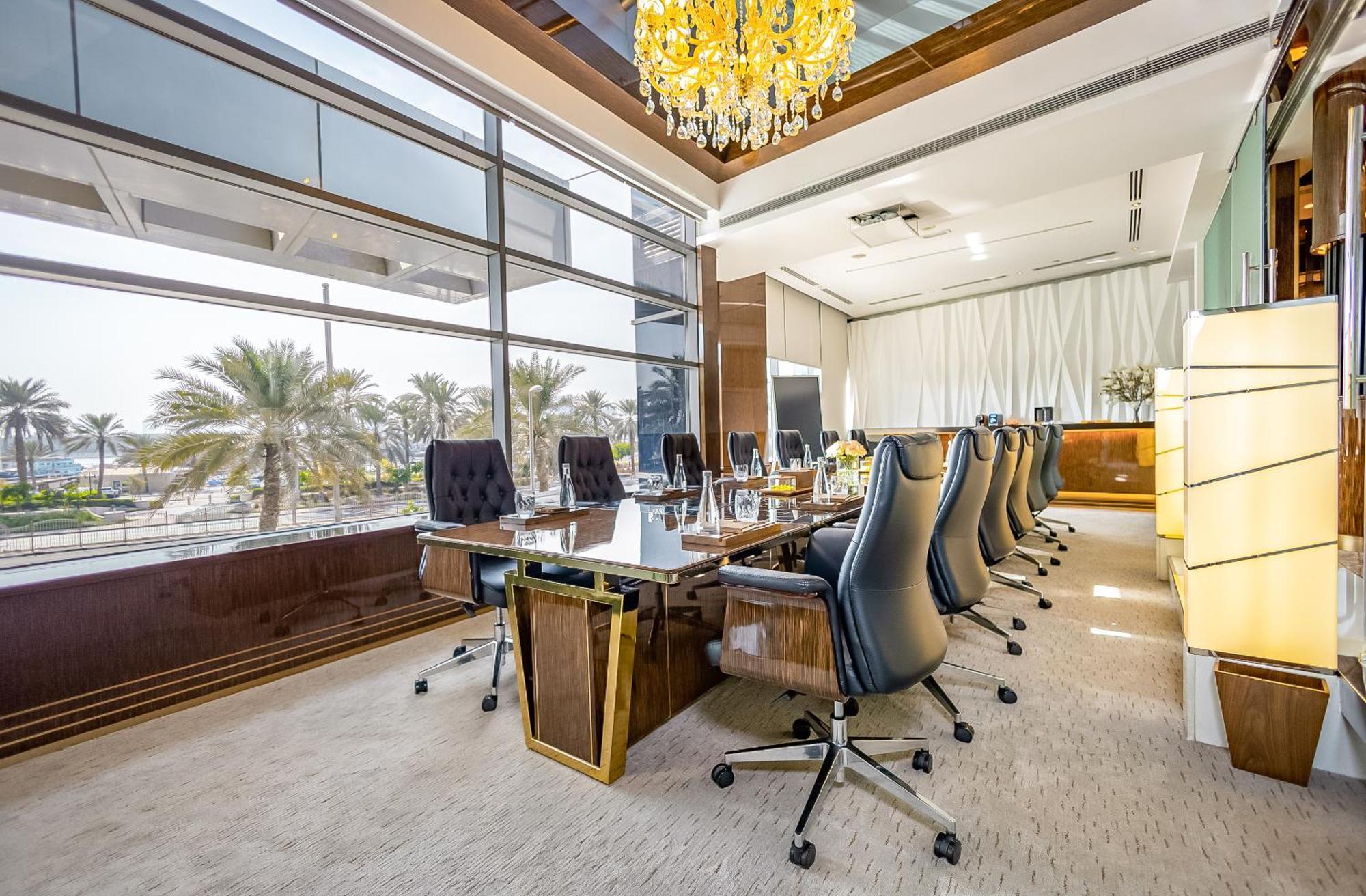 Golden Sands Boutique Hotel-Dubai Creek Екстериор снимка The photo shows a spacious, modern conference room. It features a long, polished wooden table surrounded by several high-backed chairs. The room has large windows that allow natural light to flood in, offering a view of palm trees outside. A luxuriou