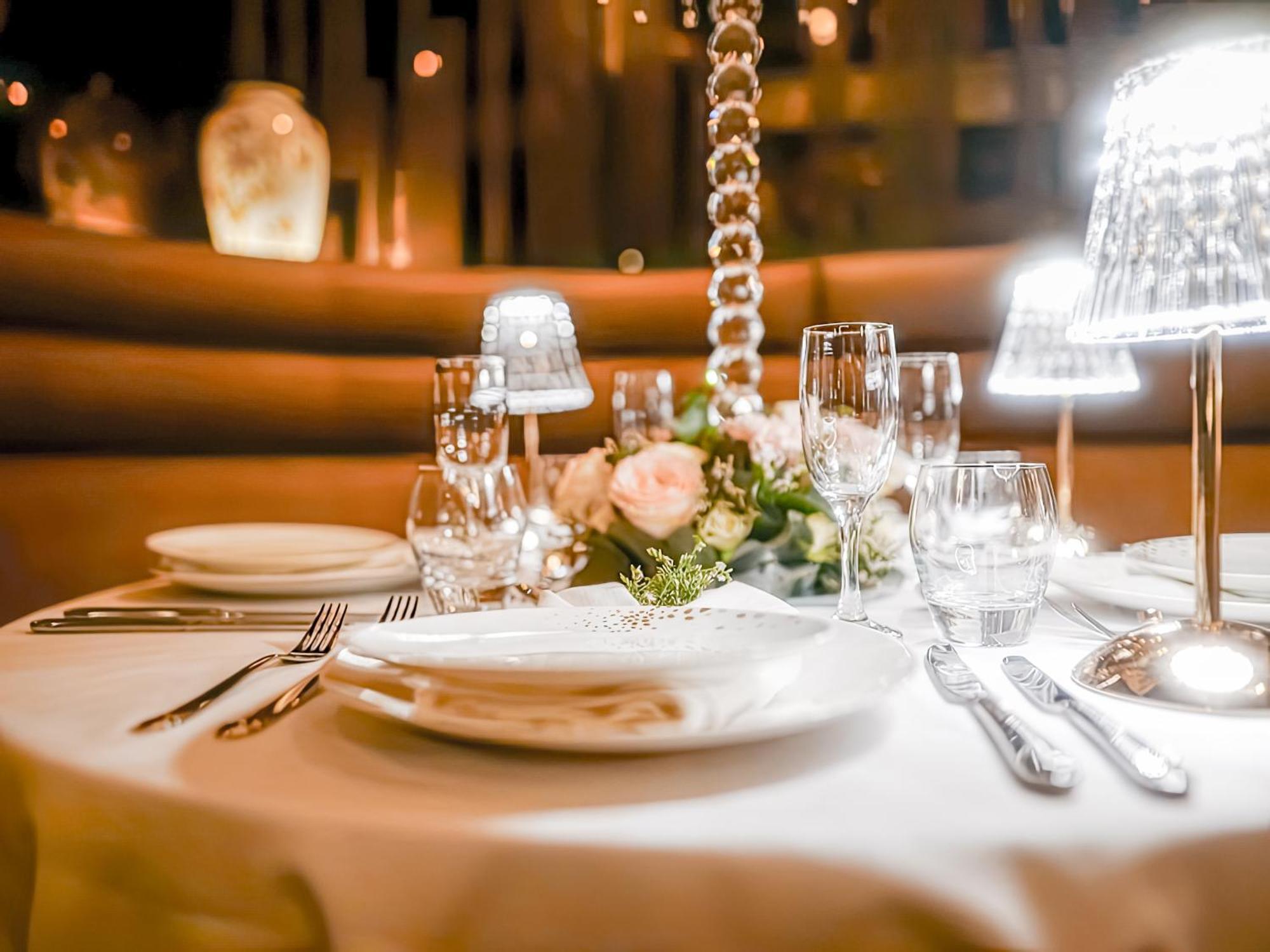Golden Sands Boutique Hotel-Dubai Creek Екстериор снимка The photo depicts an elegantly set table in a restaurant, featuring a white tablecloth. The table is adorned with decorative elements, including a floral arrangement with roses and greenery. There are multiple glassware items, such as wine glasses an