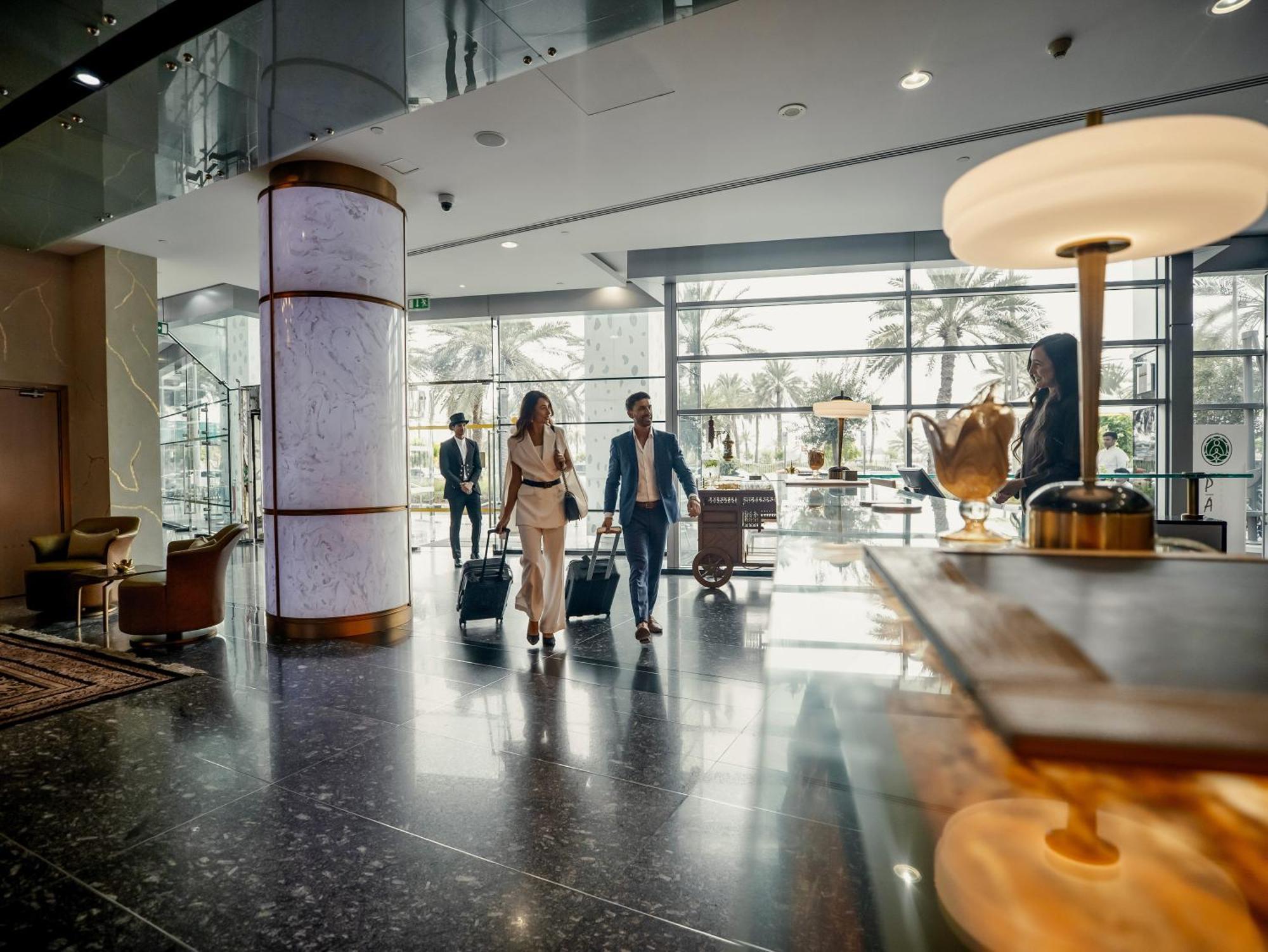 Golden Sands Boutique Hotel-Dubai Creek Екстериор снимка The photo depicts a modern hotel lobby. There are several people in business attire walking through the space, suggesting they may be arriving or checking in. The lobby features large windows that allow natural light to fill the area, and there are d