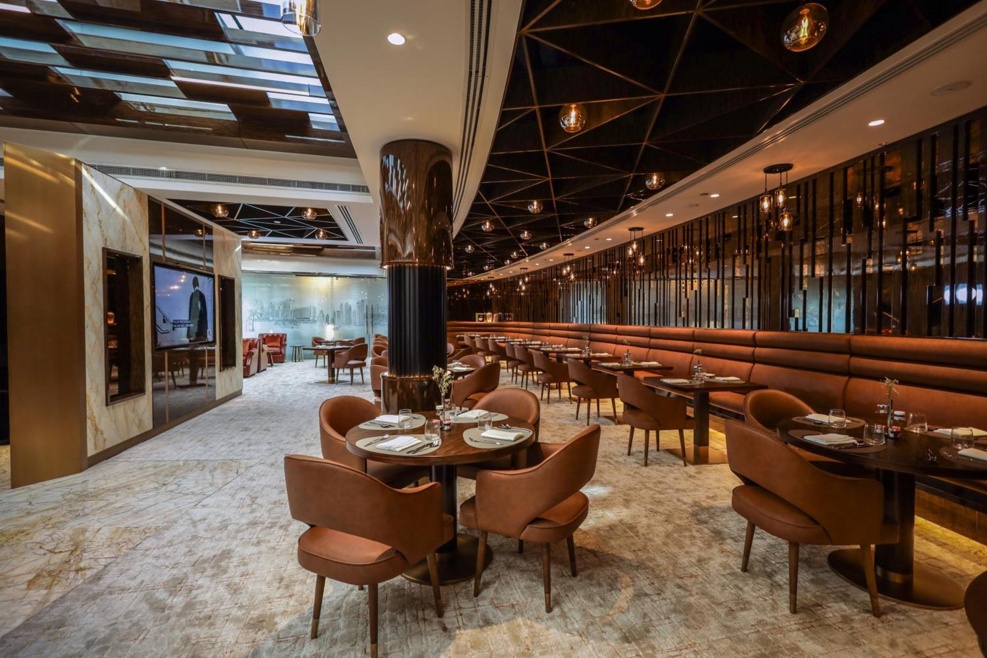 Golden Sands Boutique Hotel-Dubai Creek Екстериор снимка The photo depicts a modern restaurant interior. It features a spacious layout with a mix of seating options, including plush brown chairs and circular tables set for dining. The decor includes elegant lighting fixtures hanging from the ceiling and a 
